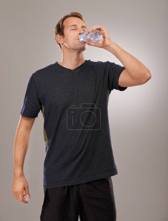 Photo for Healthy, studio or man drinking water for fitness, hydration or workout break isolated on grey background. Tired person, training or thirsty athlete with fresh h2o liquid drink for exercise or detox. - Royalty Free Image