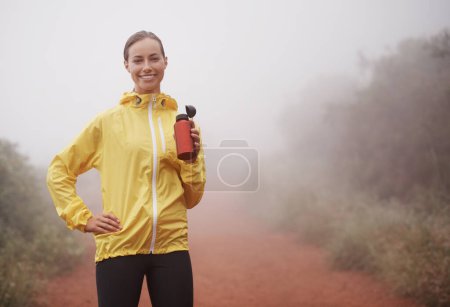 Téléchargez les photos : Nature, forme physique et portrait d'une femme buvant de l'eau pour courir sur un chemin de terre avec entraînement au marathon. Sport, entraînement et athlète dégustant une boisson pour l'hydratation sur l'exercice cardio en plein air brumeux - en image libre de droit