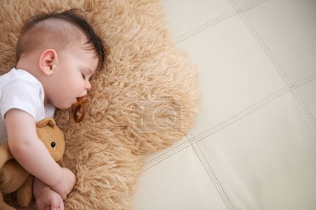 Photo for Baby, sleep and cuddle with teddybear on couch at home, rest and relax with dummy and dream. High angle, toddler, and nap in sofa for child development, growth and innocent with peace for bedtime - Royalty Free Image