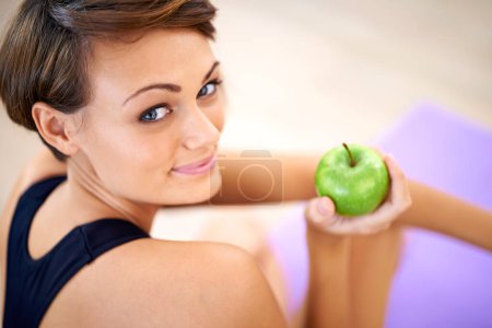 Téléchargez les photos : Portrait, exercice et femme heureuse avec pomme dans la salle de gym pour l'alimentation, la nutrition et le bien-être avec un corps sain. Visage, fitness et personne mangeant des fruits pour la vitamine c ou les bienfaits des aliments biologiques sur tapis de yoga. - en image libre de droit