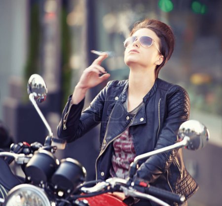 Foto de Mujer, cuero y cigarrillo en la ciudad con moto para viajar, transporte o viaje por carretera como rebelde. Moda, calle y persona fumar nicotina con actitud en bicicleta clásica o vintage para el viaje. - Imagen libre de derechos