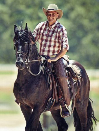 Foto de Retrato, vaquero y hombre a caballo con silla de montar en el campo en el campo para equitación o entrenamiento. Naturaleza, verano y sonrisa con jinete maduro en animal en rancho al aire libre en Texas rural. - Imagen libre de derechos