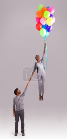 Photo for Balloon, flying and couple in studio for growth, celebration and present on gray background. independant, opportunity and isolated man and woman holding hands with inflatable for party and surprise. - Royalty Free Image