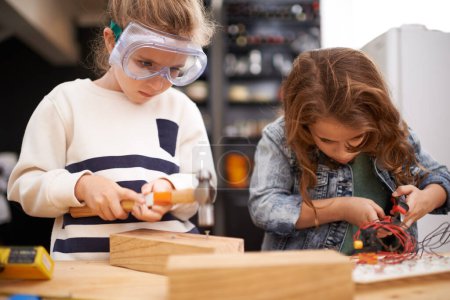 Photo for Children, construction and diy in workshop with tools, play and game in kitchen of home. Girls, hammer and safety glasses for wood project or building, carpentry and woodworking or manufacture. - Royalty Free Image