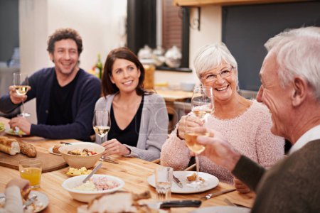 Téléchargez les photos : Sourire, acclamations et famille au dîner dans la salle à manger pour la fête, la célébration ou l'événement à la maison moderne. Heureux, collant et groupe de personnes profitant du repas, souper ou déjeuner avec du vin à la maison - en image libre de droit