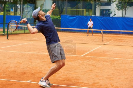 Photo for Exercise, sports and tennis with man serving on clay court to start competition or game from back. Fitness, training or workout and athlete man with racket in stadium or venue at beginning of match. - Royalty Free Image