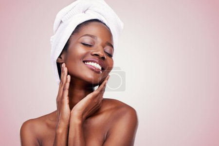Haare, Handtuch und glückliche schwarze Frau im Studio für Hautpflege, Wellness oder Körperpflege auf rosa Hintergrund. Schönheit, Reinigung und Hände im Gesicht eines afrikanischen weiblichen Modells mit kosmetischer, glänzender oder glühender Haut.