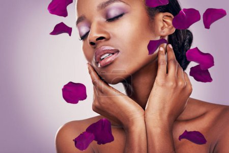 Photo for Flower, petal and black woman in studio for makeup, beauty or wellness on purple background. Floral, skin and Africa model with soft cosmetics, shine or organic transformation with lavender aesthetic. - Royalty Free Image