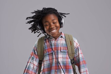 Téléchargez les photos : Homme noir, musique et sourire d'un adolescent avec hip hop et rap audio dans un studio. Détendez-vous, sac à dos et étudiant avec écouteurs diffusant une chanson radio avant l'école avec un enfant heureux et fond gris. - en image libre de droit