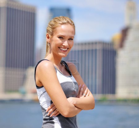 Foto de Retrato, mujer y feliz en la orilla del río con la ciudad en ropa deportiva para caminar, fitness y mentalidad saludable en Nueva York. Persona segura, femenina y sonriente con autocuidado en verano y clima caluroso. - Imagen libre de derechos