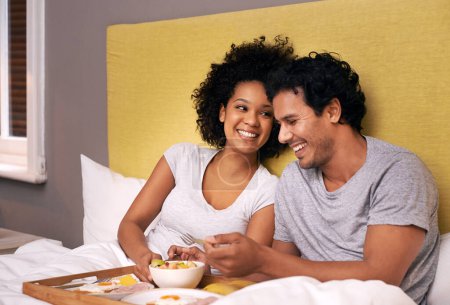 Photo for Couple, smile and bedroom for breakfast on tray for wakeup, morning and food for eat, rest and relax. Diverse and young people and laugh with happiness for bonding with fruit and bowl for joy. - Royalty Free Image