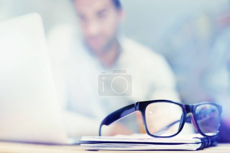 Photo for Blur, notebook and glasses on desk with man in office for planning, schedule and agenda on table. Laptop, eyewear or worker copywriting with diary journal for business, administration or email on web. - Royalty Free Image