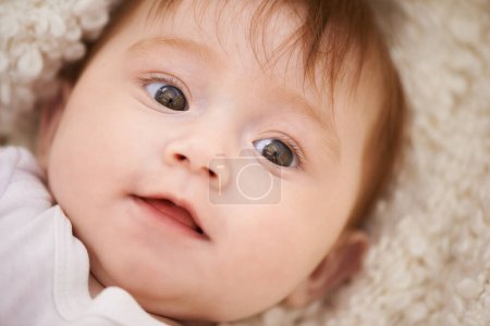 Foto de Feliz, lindo y primer plano del bebé en manta jugando para el desarrollo del niño y la cara curiosa. Sonríe, niña dulce y joven, bebé o recién nacido relajante y acostado en la cama en la habitación del vivero en casa - Imagen libre de derechos