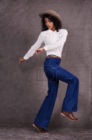 Photo for Woman, fashion and western clothes in studio, wild west and country style on Indian model. Jumping, confident strong female person with trendy hat accessory, culture and isolated on backdrop. - Royalty Free Image