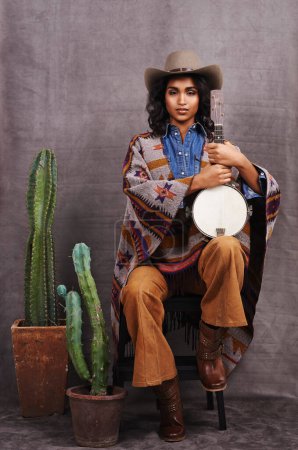 Photo for Portrait, cowgirl or woman with instrument for music in studio and cool fashion or clothing on grey background. Native American person, western and model with plants, boho style and banjo for a song. - Royalty Free Image
