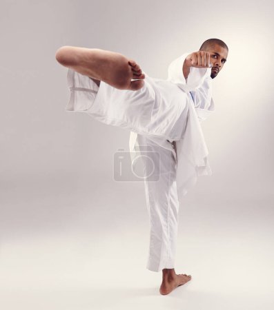 Photo for Karate, exercise and man kick in portrait on studio, white background or mockup of martial arts. Serious, warrior and training to fight with foot and punch fist with power in competition for sport. - Royalty Free Image