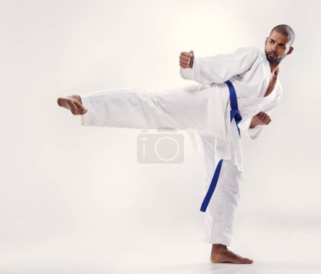 Photo for Man, kick and karate fighter in studio, fitness and martial arts on white background. Black male person, athlete and blue belt for taekwondo, discipline and warrior ready for self defense or battle. - Royalty Free Image