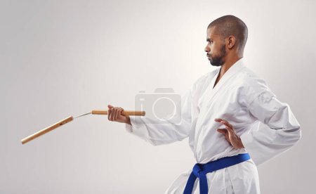 Photo for Nunchucks, karate and man in martial arts fight with weapon in training for defence in white background of studio. Nunchaku, exercise and fighting with equipment in sport with skill and power in club. - Royalty Free Image