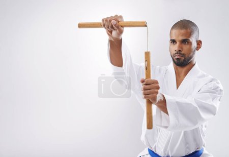 Nunchucks, karate and man in martial arts fight with weapon in training for defence in white background of studio. Nunchaku, exercise and fighting with equipment in sport with skill and power in club.