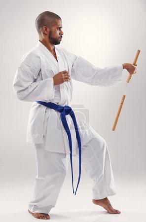 Nunchaku, karate and man in martial arts fight with weapon in training for defence in white background of studio. Nunchucks, exercise and fighting with equipment in sport with skill and power in gym.