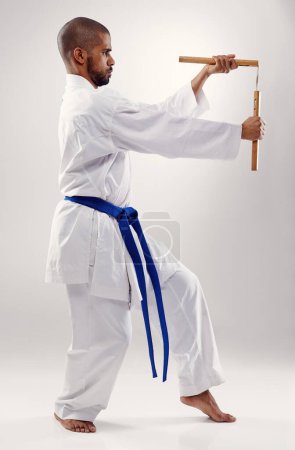 Karate, Kampf und Mann mit Nunchaku in den Kampfkünsten, im Studio oder im Training mit der Waffe zur Verteidigung auf weißem Hintergrund. Nunchucks, Übung und Kampf mit Geräten im Sport mit Geschick und Kraft.