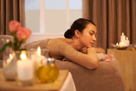 Photo for Woman, candle and relax on massage table at hotel for aromatherapy, stress relief and holistic treatment. Female person, peace and zen at spa for body health, self care and spiritual healing. - Royalty Free Image