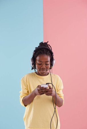 Photo for Teen, boy and relax with phone and headphones in studio for listening to music in high school and reading. Happy, kid and creative post on social media with audio and watch live stream on app. - Royalty Free Image