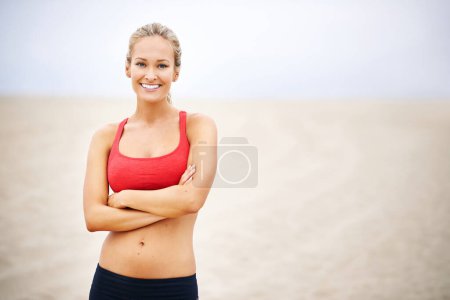 Femme, portrait et fitness sur la plage de sable avec les bras croisés, confiant et sourire avec bien-être et en plein air. Exercice, athlète et sport avec bonheur pour la santé, marathon ou course pour l'entraînement cardio.