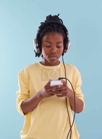 Photo for Phone, music and black boy with headphones in studio for internet, playlist or search on blue background. Smartphone, radio and teen model with app for podcast, streaming or sign up subscription. - Royalty Free Image