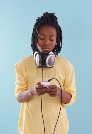 Photo for Music, headphones and black kid in studio for internet, playlist or track search on blue background. Smartphone, radio and African teen boy with app for podcast, streaming or sign up subscription. - Royalty Free Image