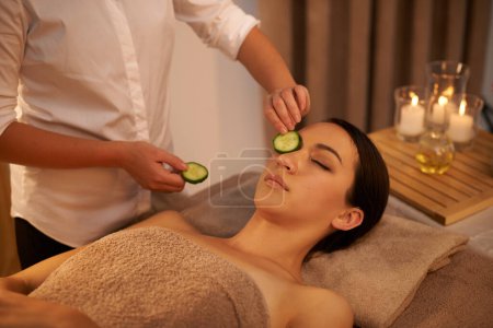 Photo for Face, massage therapist and woman with cucumber in spa for peace, relax or wellness. Facial, salon or hands apply vegetable on eyes for natural beauty, skincare or healthy organic treatment with mask. - Royalty Free Image