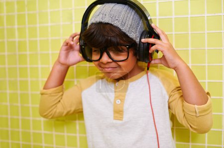 Foto de Niño, música y gafas con auriculares en el baño con canción en un hogar. Radio, gafas y moda juvenil con un chico hipster escuchando audio con estilo cool en una casa con marcos de gafas. - Imagen libre de derechos