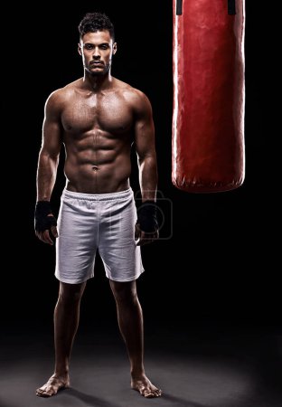 Téléchargez les photos : Studio, boxeur et portrait d'homme, sac de boxe et gants pour l'entraînement avec force et muscle. Adulte, athlète et homme dans un fond sombre, sain et puissant avec le corps, le travail et le sport. - en image libre de droit