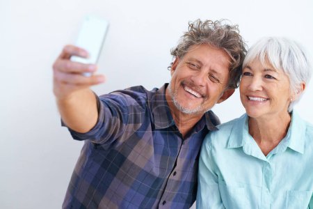 Téléchargez les photos : Vieux couple, selfie et heureux ensemble pour le message sur les médias sociaux, la mémoire et l'amour avec joie sur fond blanc. Confiance, soutien et loyauté envers les personnes mariées, sourire dans l'image pour la poste et l'application mobile. - en image libre de droit