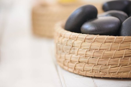 Photo for Stone, massage and closeup on basket in spa for luxury service in hospitality at hotel on holiday or vacation. Rocks, container and object for wellness treatment on table or detail of pebble. - Royalty Free Image