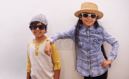 Photo for Children, portrait and fashion or sunglasses for style and looking cool on a wall or white background at home. Happy sibling, girl and boy with trendy clothes, casual and shades for fun or confidence. - Royalty Free Image
