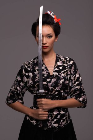 Foto de Mujer asiática, moda y espada en estudio sobre confianza con fondo gris, estilo tradicional y elegante. Retrato, persona japonesa y femenina con diseñador, moda y atuendo para la herencia. - Imagen libre de derechos
