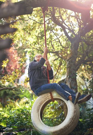 Boy, tyre swing and playing in garden with happiness, recreation or countryside vacation in summer. Child, excited and diy adventure playground in backyard of home with sunlight and trees in nature.