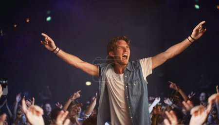 Photo for Riding a wave of fans. An excited young man cheering atop a friends shoulders as his favourite band plays - Royalty Free Image