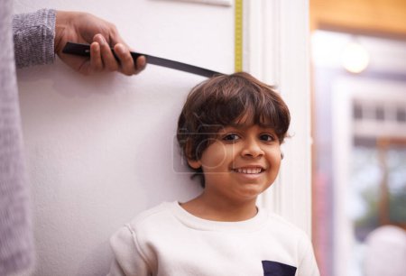 Photo for Child, portrait and measure height growth with ruler for childhood development, taller or elementary school. Boy, student and face with hand or tape at wall in apartment for checking, size or happy. - Royalty Free Image