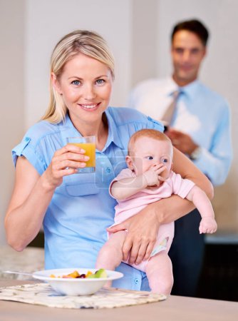 Photo for Portrait, mother and baby with juice and breakfast in the morning with businessman leaving for work. Woman, food and eating fruit with little child or kid for healthy diet and father in background. - Royalty Free Image