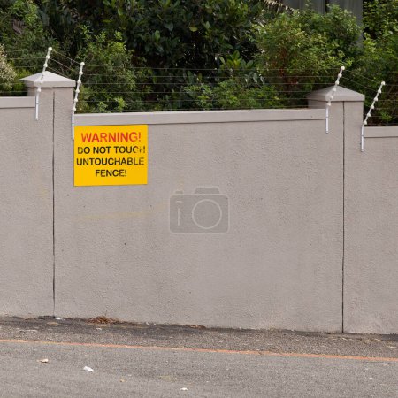 Electrical fence, warning and sign on wall of property for caution, notification and information. Public signage, symbol and building with board, poster and for attention, message and safety message.