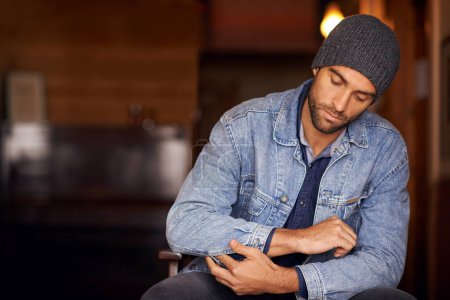 Photo for Man, trendy and winter fashion in home, house and hipster with serious male person sitting in warm clothes. Beanie, head wear for comfort, indoor and fixing denim jacket for urban trends in Canada. - Royalty Free Image