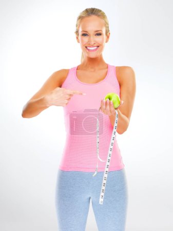 Photo for Woman, portrait and apple with measuring tape for healthy weight loss or hungry, wellness or white background. Female person, face and pointing at fruit in studio or training routine, diet or mockup. - Royalty Free Image