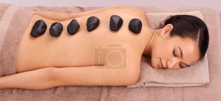Photo for Calm, hot stone and woman with back massage at spa for wellness, self care and grooming treatment for healing. Skin, girl and high angle of person with warm rock body routine on table for zen - Royalty Free Image