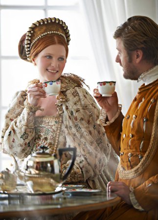 Photo for King, queen and couple with tea for royalty, smile and conversation in vintage clothes with style in castle. Woman, man and drink together in morning with Victorian fashion at regal palace in UK. - Royalty Free Image