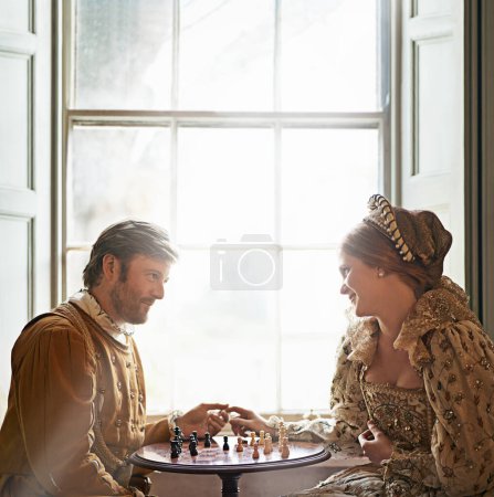 Renaissance, couple et date d'échecs dans la maison avec la main tenant, costume vintage et médiéval dans un palais. Fenêtre, luxe et reine avec sourire du jeu de stratégie et parler avec amour et soin.