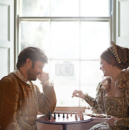 Renaissance, couple et échecs à la maison avec royauté, costume vintage et médiéval dans un palais. Fenêtre, luxe et reine avec sourire du jeu de stratégie et de parler tout en jouant avec l'amour.