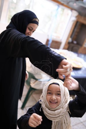 Téléchargez les photos : Musulman, maman et enfant à la maison jouant à un jeu et dansant dans le salon avec bonheur dans la famille islamique. excité, fille et mère dans la maison ensemble tenant la main avec énergie dans le mouvement de rotation. - en image libre de droit