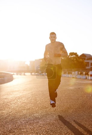 Photo for Man, running and martial arts in street for exercise, training and cardio for health, stamina and tattoo in sunshine. Fighter, outdoor and road for workout in morning, sunrise and mma for wellness. - Royalty Free Image
